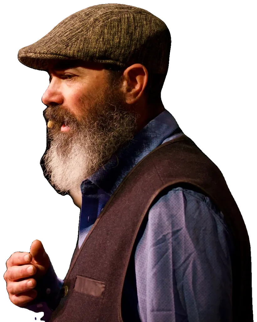Tevye, gray bearded in a flat cap, presses a fist to his chest as he speaks with conviction.