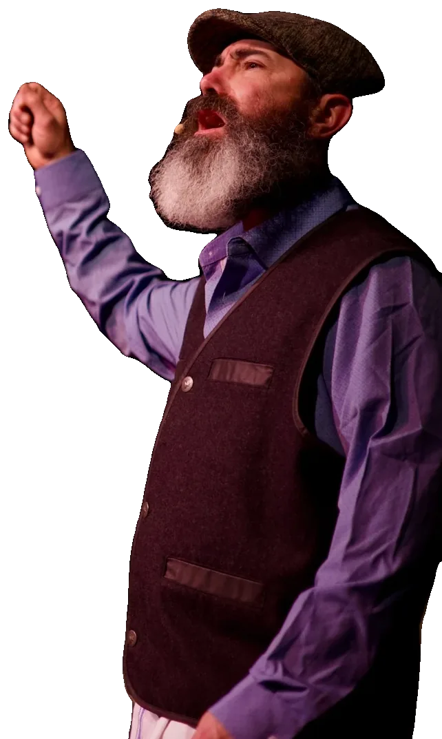 Tevye, in a flat cap and vest, raises his fist toward the sky as he sings.