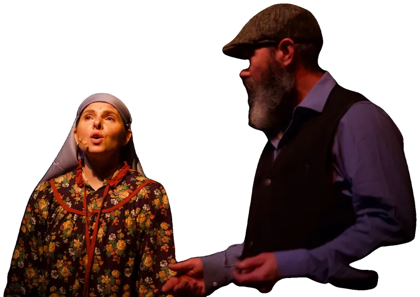 Golde, in a floral dress and headscarf, sings beside Tevye as he reaches out to her.