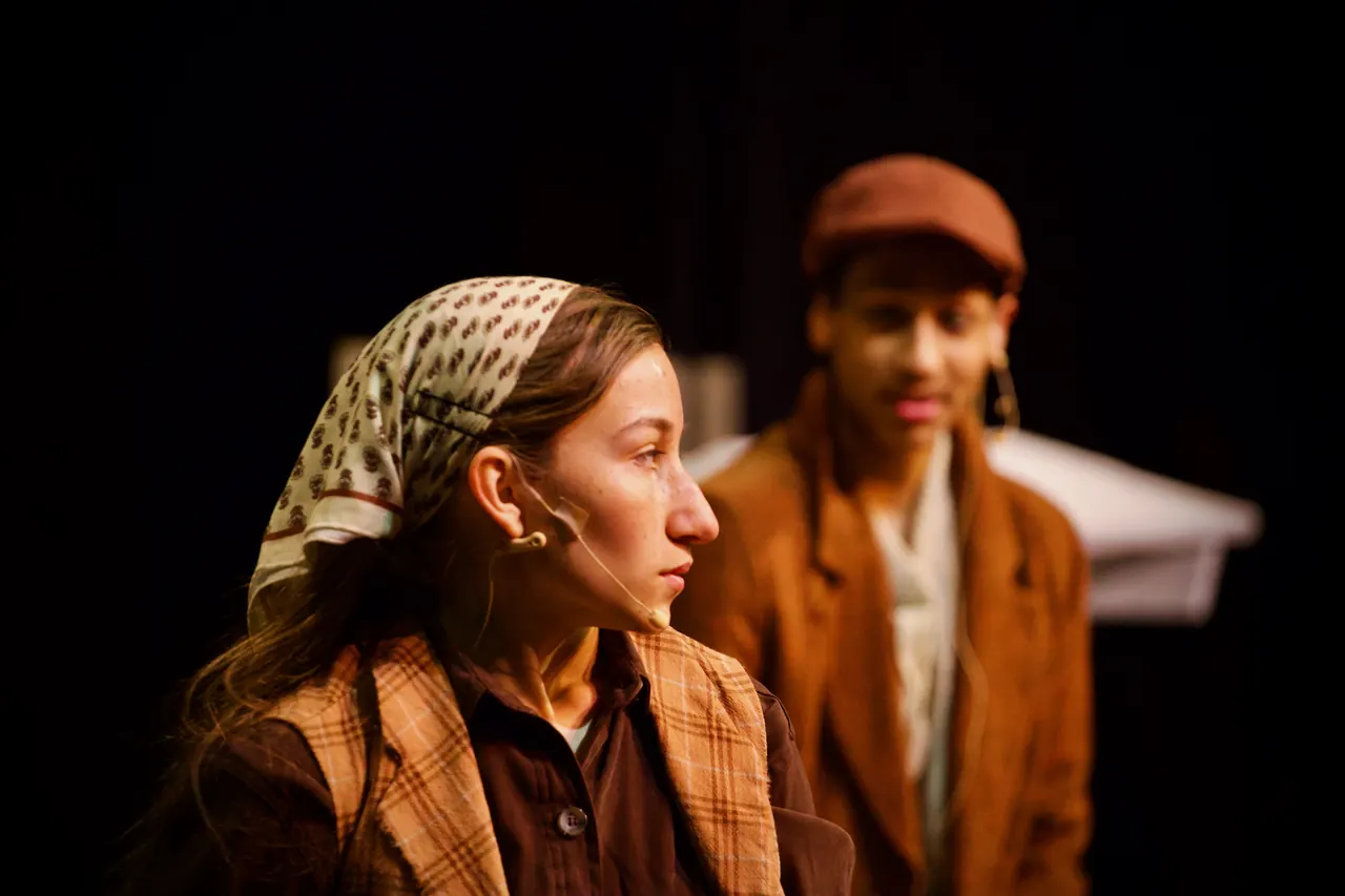 A young woman in a headscarf listens intently while a young man in a cap stands behind her.