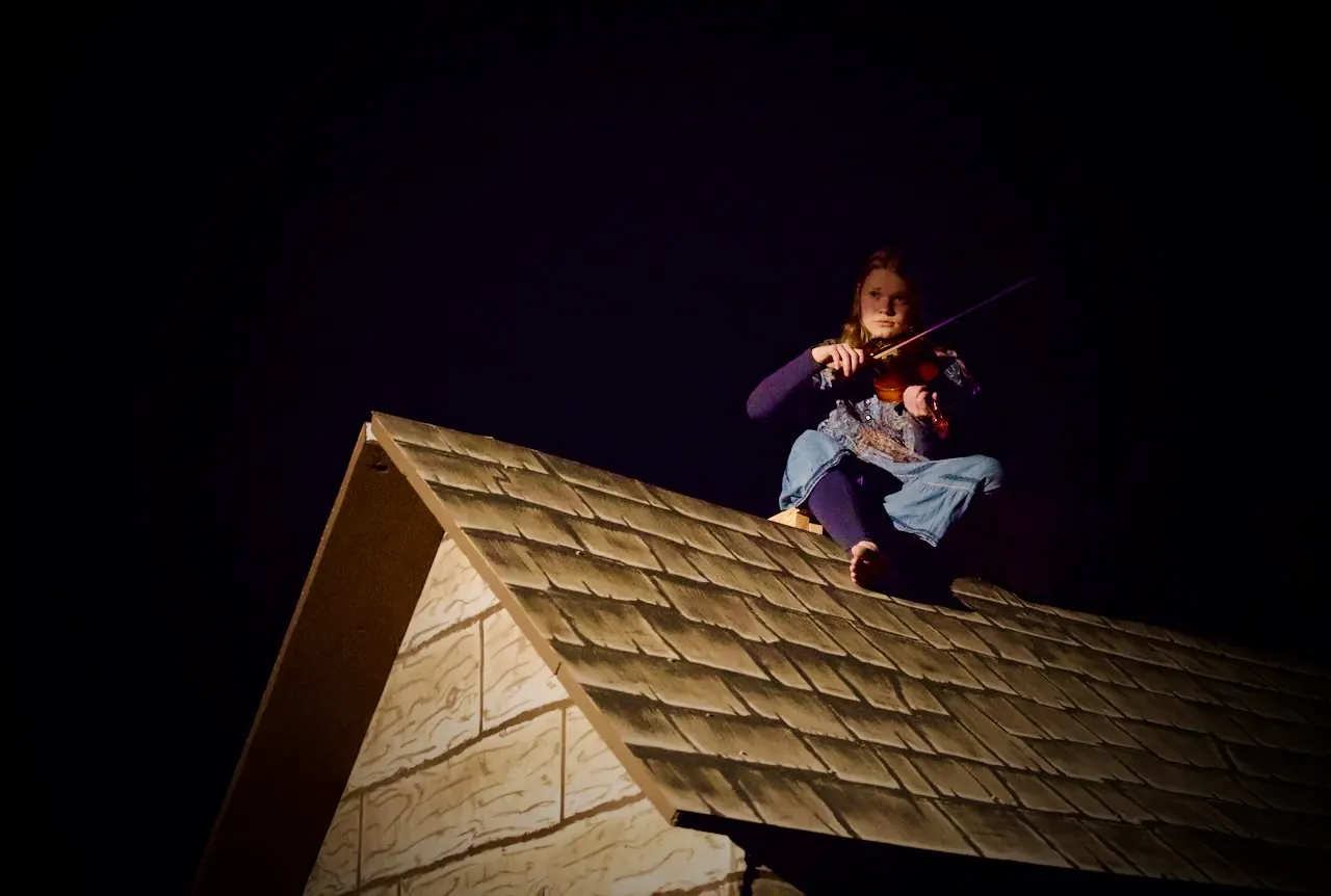 The fiddler plays his violin while perched on a cottage rooftop.