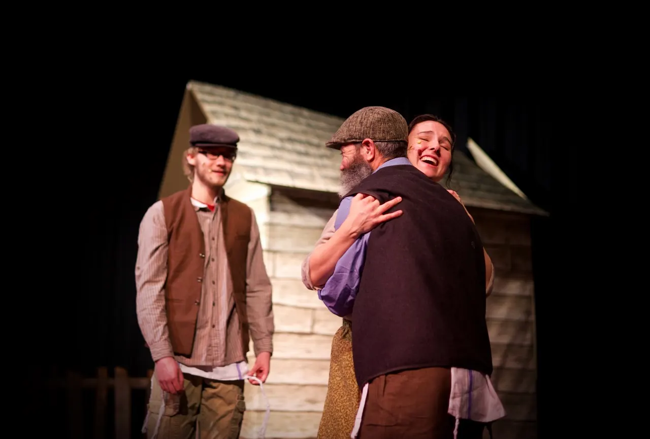 Tevye pulls a young man into a joyful embrace.