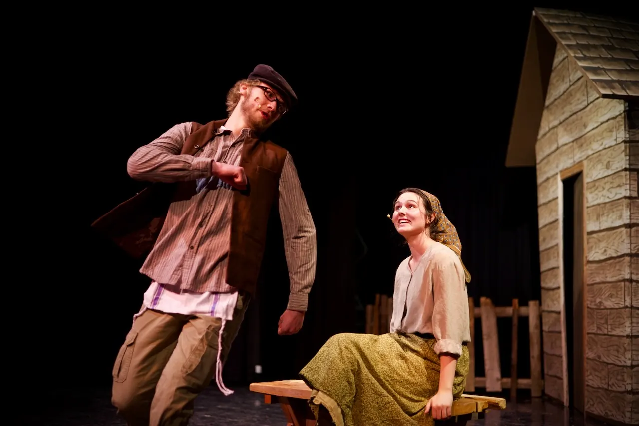 A young man throws his arms back in delight while a young woman laughs on a bench.