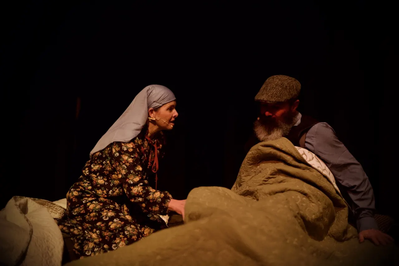 Golde and Tevye sit up in bed, deep in conversation.